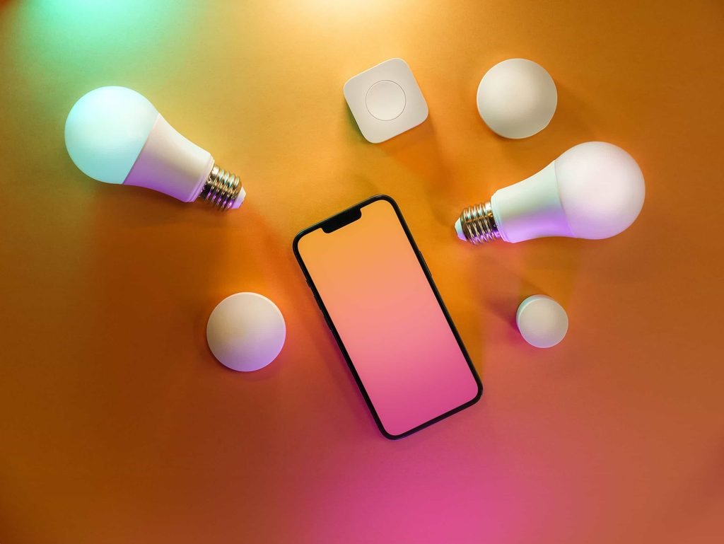Smart lighting ecosystem with two smart LED bulbs and a smartphone on a gradient background.